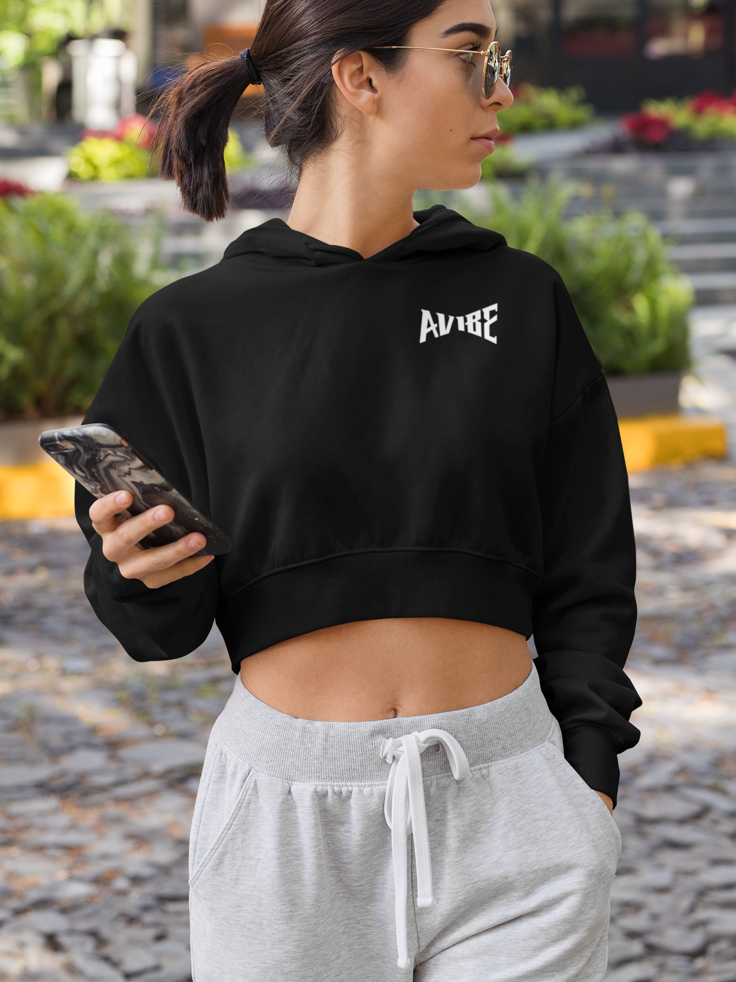 Woman wearing a black hoodie with 'ALIVE' text and gray sweatpants, holding a phone outdoors.