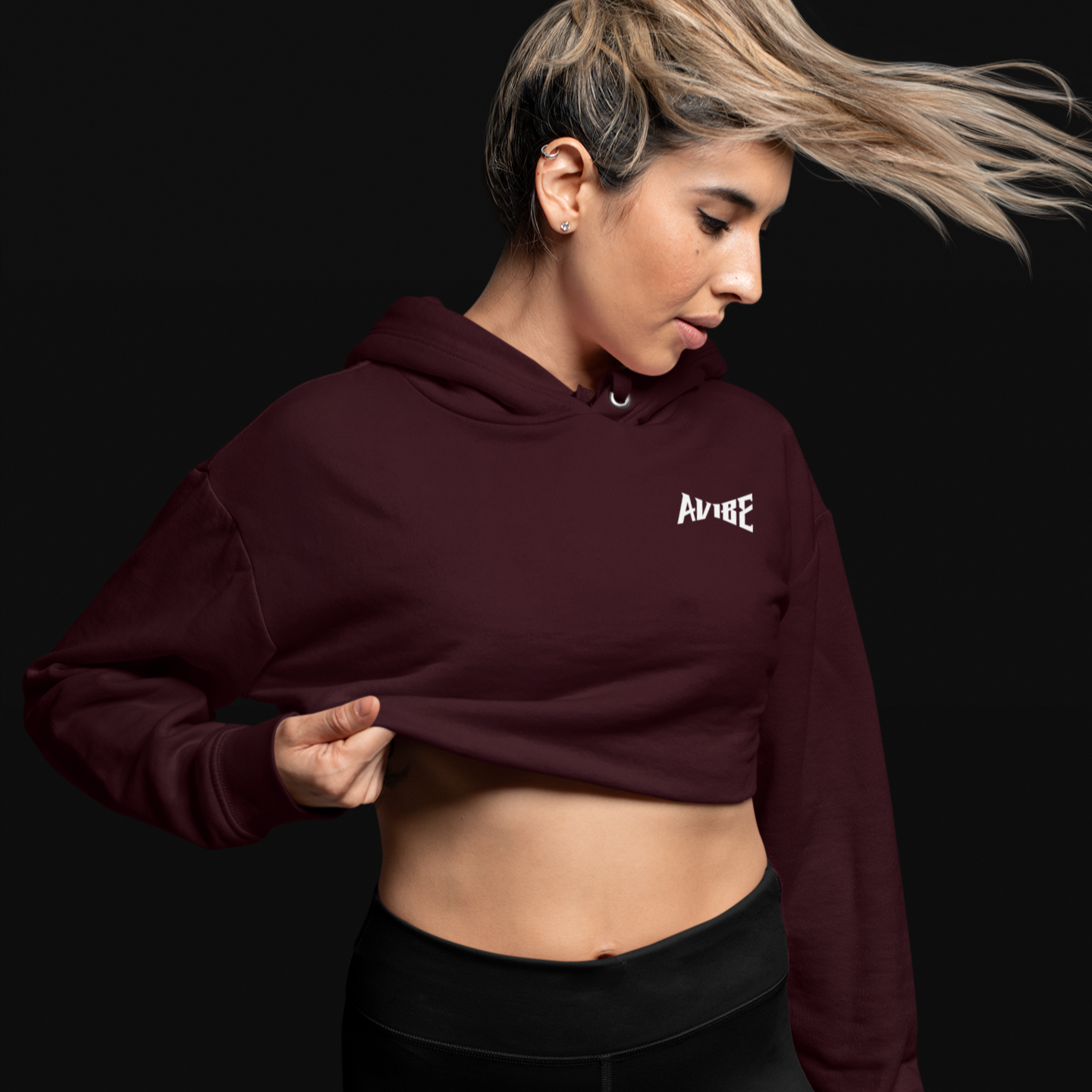 Woman wearing a maroon hoodie with a logo and black shorts on a black background