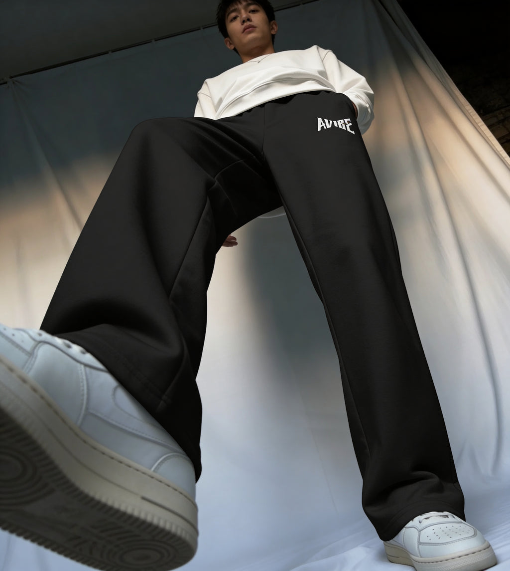 Person wearing black pants with a brand logo and white sneakers on a neutral background