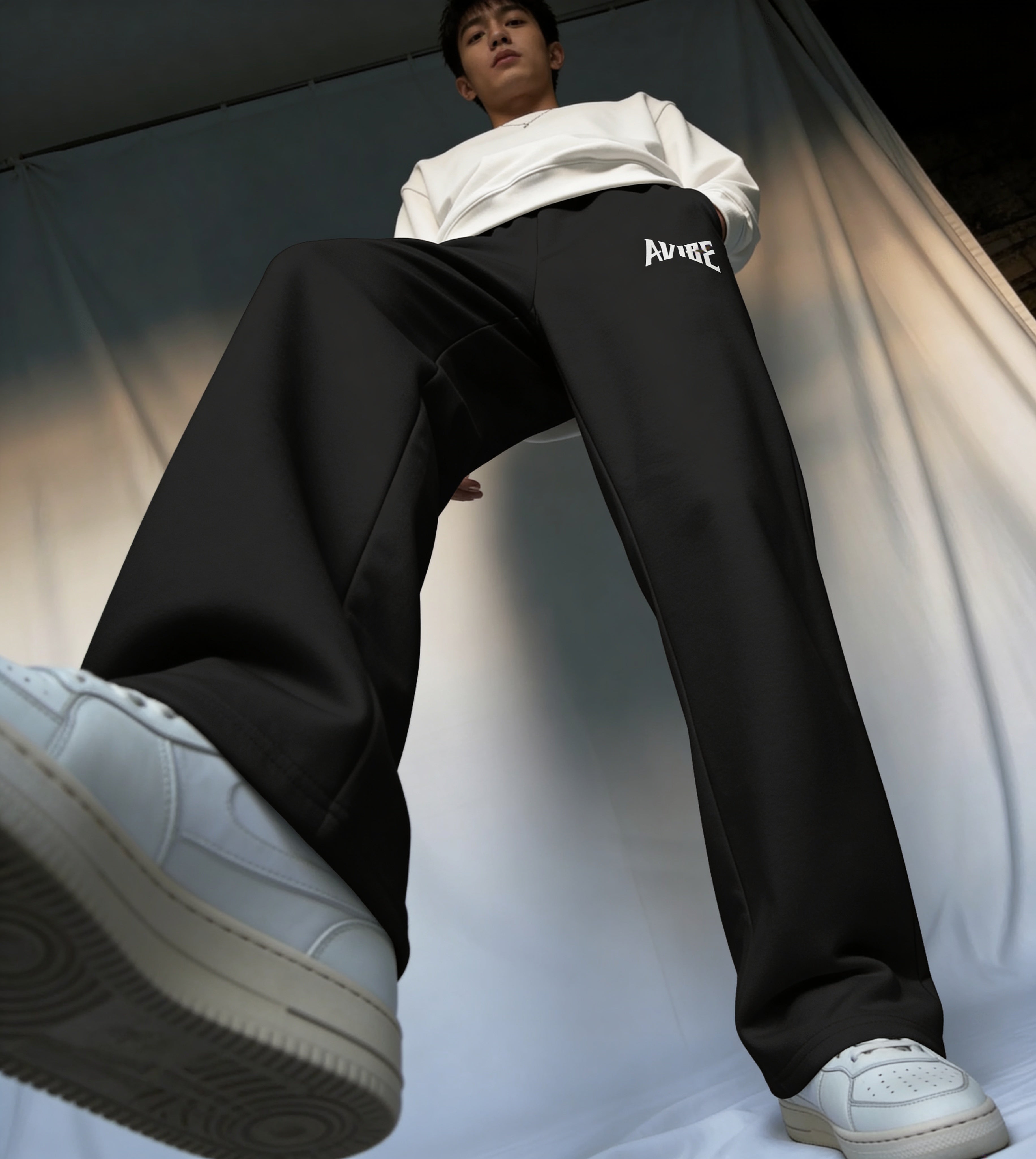Person wearing black pants with a brand logo and white sneakers on a neutral background